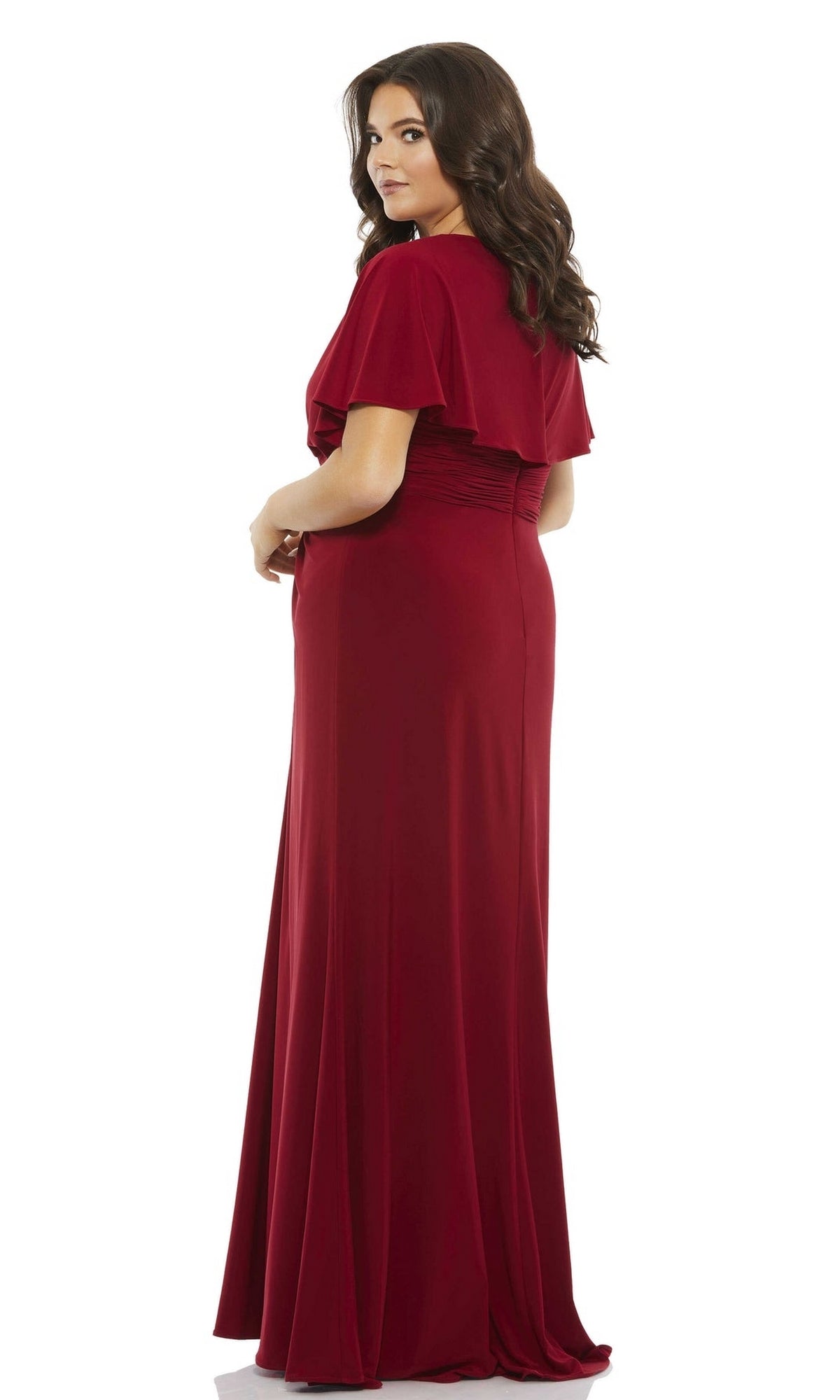 A woman with long brown hair wears the Long Plus-Size Prom Dress 67916 by Mac Duggal, a floor-length, short-sleeve deep red formal gown, and stands facing slightly away against a white background.